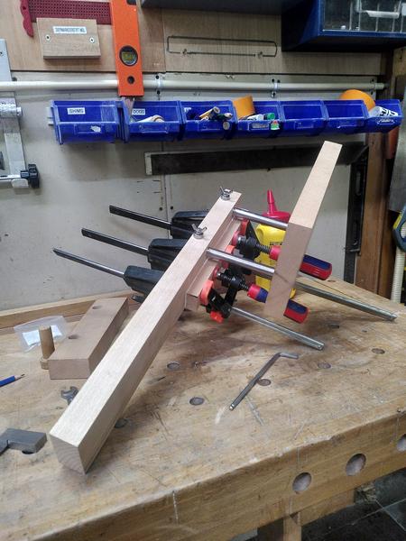 A varied assortment of clamps and metal work and pieces of beech wood
(fagus sylvatica) on a work bench. The assembly is sligthly off the bench
at an angle. A yellow pot of glue is in the background.