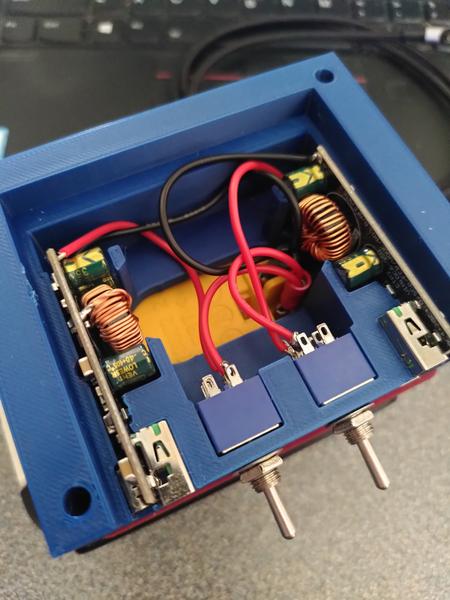 A blue 3d printer cuboid shape. The recess in side is filled with two
circuit boards. Each board has a large coil shaped inductor there's some
black and red wires that go down to a yellow part below. Two blue switches
are mounted to the front